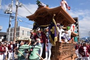 神輿の上の法被を着た男性に祝い樽を渡している写真