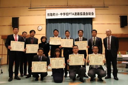 感謝状を手に持ったスーツ姿のPTA役員の方たちと町長が2列に横並びに並んでいる記念写真