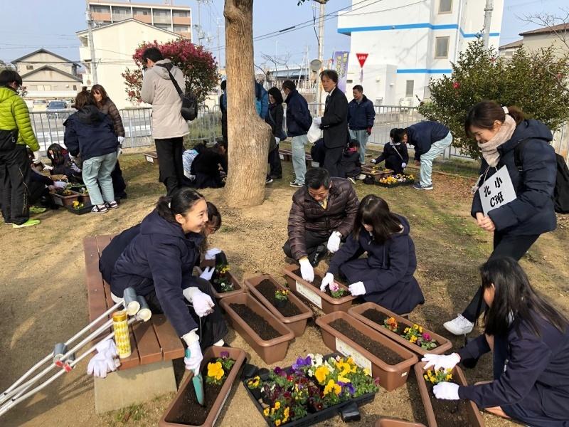 9個の茶色のプランターが中央に置かれていて、学生や町長たちがパンジーなどの花を植えている写真