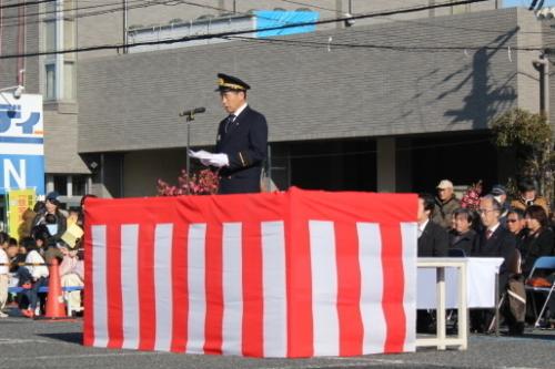 紅白の幕がかけられた台の上で消防の制服姿の町長が白い紙を見ながら話をしている写真