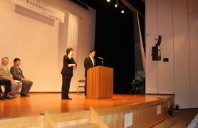 舞台上の講演台で話をする町長、隣に手話で通訳をする女性の様子を斜め下から撮影した写真