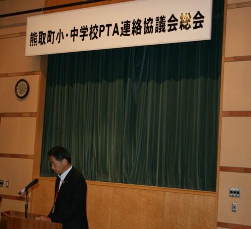 舞台の前に置かれた演台の前で立ちながら話す町長を左側から写した写真