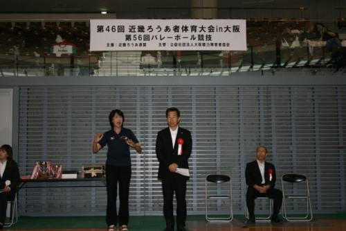 バレーボール競技の開会式にて前に立って話す町長と、横に立つ手話通訳女性の写真