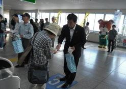駅の構内で町長が紙袋を持って、帽子を被った通行人の女性にティッシュを配って啓発活動をしている写真
