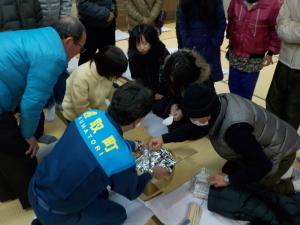 銀色の袋に入った防災食の説明をする職員と、その周りに集まり話を聞く参加者の写真