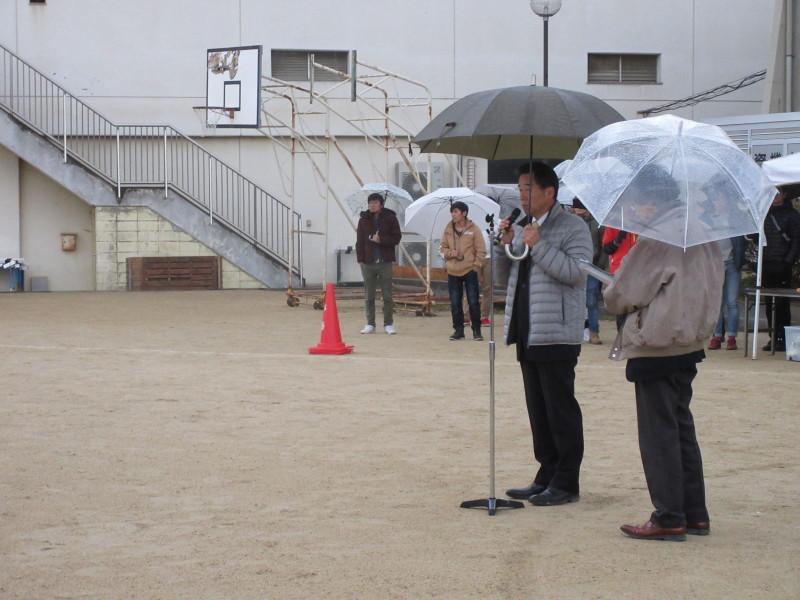 町長がグランドに立ち、傘を左手にマイクを右手に持って話をしている様子が写っている写真