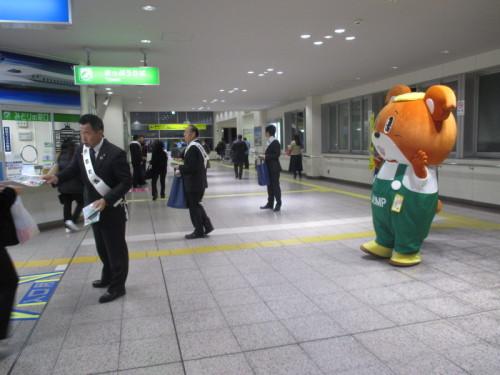 駅構内でチラシを配布しながら啓発を行う町長と男性達の後ろにゆるキャラが手を挙げている写真