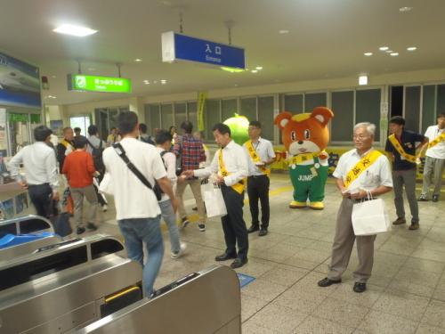 駅の構内で交通安全と書かれた黄色いタスキをかけた町長が通行人にティッシュを配っている写真