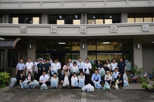 熊取町役場の前で、笑顔で拾ったごみを持つ町長と参加者職員の集合写真