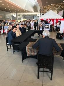 奥には紅白の幕がかかったテント、手前には黒いテーブルの椅子に腰かける千玄室氏と参加者達が写っている写真