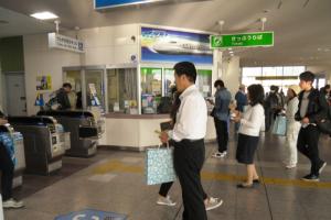 駅の改札前で水色の紙袋を持った男女がティッシュ配りを行っている様子の写真