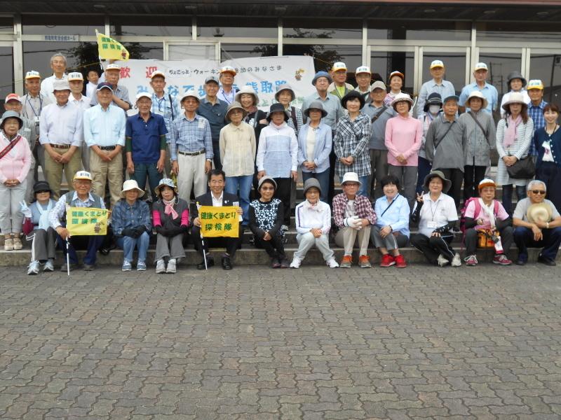 健康くまとり探検隊と書かれた黄色い旗を持った町長が中央に座り、町長の横や後ろに参加者達が並んでいる集合写真