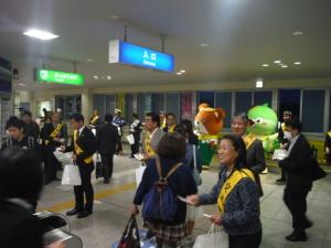 夕方の熊取駅で交通安全街頭啓発キャンペーンを行っている町長とジャンプ君メジーナちゃんなど関係者の人達の写真