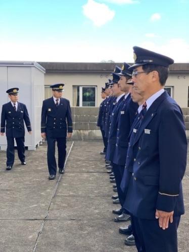 消防の制服を着た職員たちが横一列に並んでいて、その前を制服姿の町長が歩いている写真