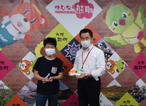 ジャンプ君とメジーナちゃんをモチーフにした折り紙の作品を持った町長と秦翔汰さんが並んで立っている記念写真