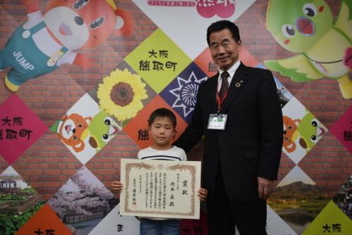 賞状を持つ男の子と、その横に立つ町長の写真
