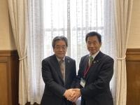 町長と田中副知事が横並びでお互いの両手を重ねて握手をしている写真