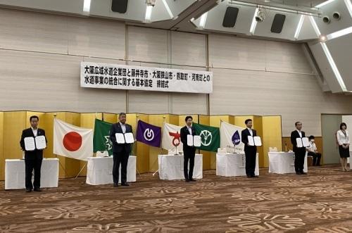 金屛風の前に日本国旗や町旗が飾られ、その前には町長と4名のスーツ姿の男性が締結書を持って並んで立っている写真