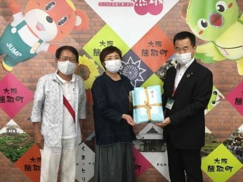 記念品を町長と女性が二人で持っていて、女性の横にメガネをかけた男性が並んで立っている写真
