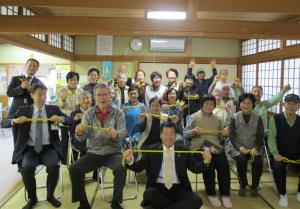 水荘園長生会の方と町長がタピオ体操のゴムを両手でのばして持ち、ポーズをとっている集合写真