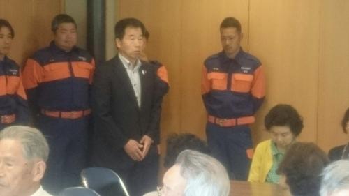 中央に町長、手前には座っている参加者達、奥には消防団員の男性達が立っている写真