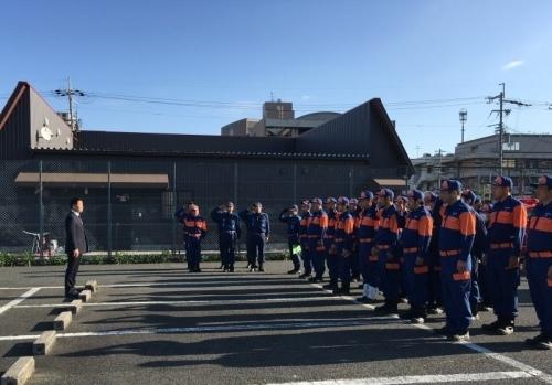 右側には大勢の消防隊員が並んでいて、左側に町長、中央には敬礼をする消防隊員が三列に並んでいる写真