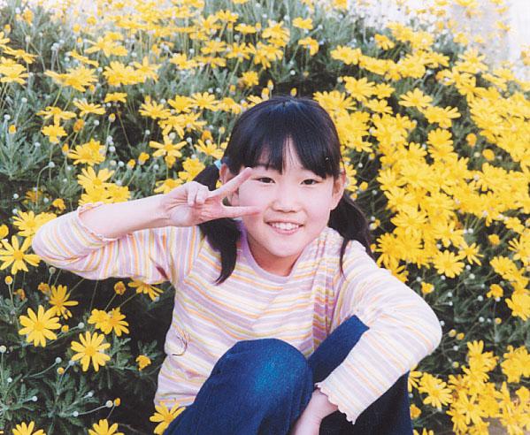 黄色い花をバックにピースサインをしている吉川ゆりさんの写真
